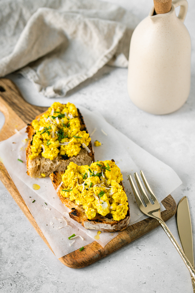 Vegan tofu scramble with on sourdough toast, topped with fresh herbs and vegan cheese.